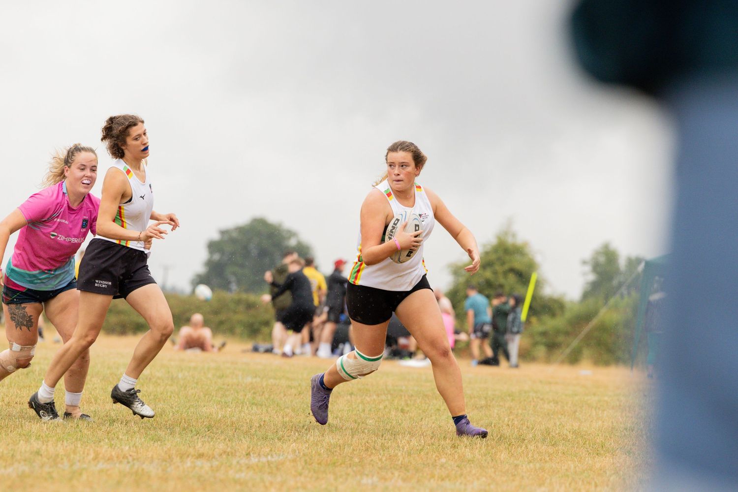 Athletes compete in an outdoor running event on a grassy field during a cloudy summer day.