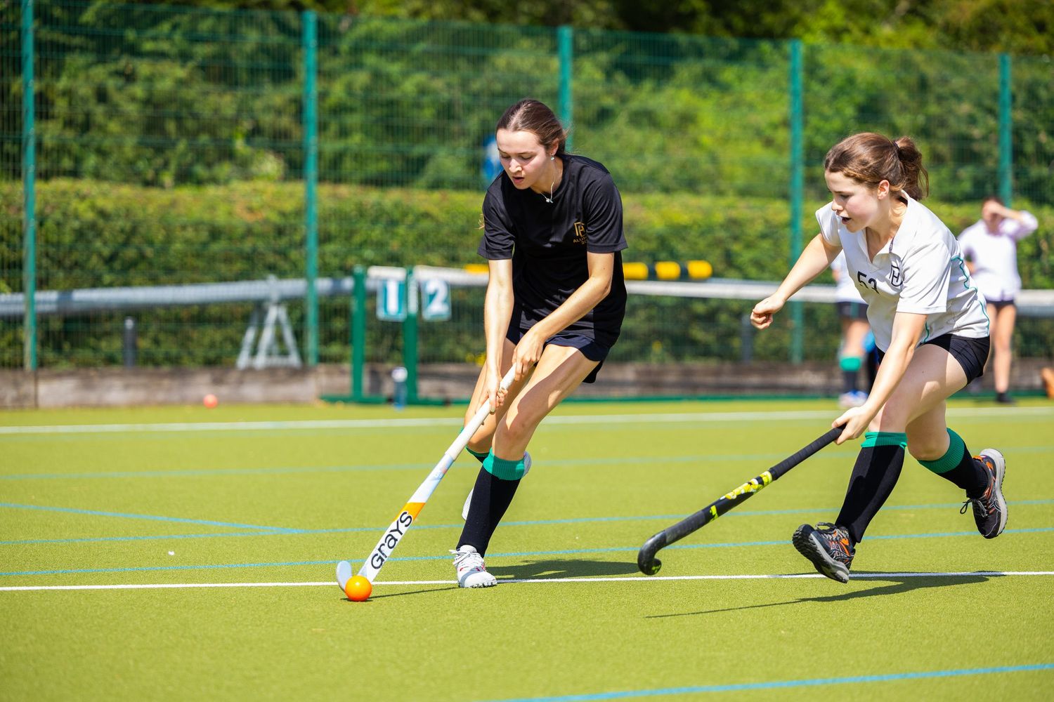 Athletes compete for ball control during field hockey match on sunny outdoor pitch.