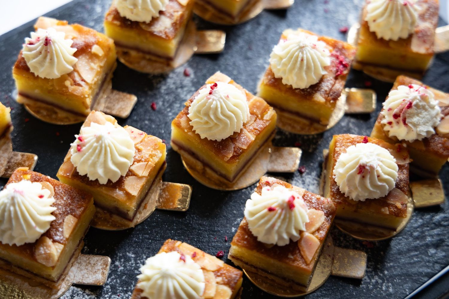 Elegant mini dessert bites with whipped cream and garnishes arranged on a dark serving platter.