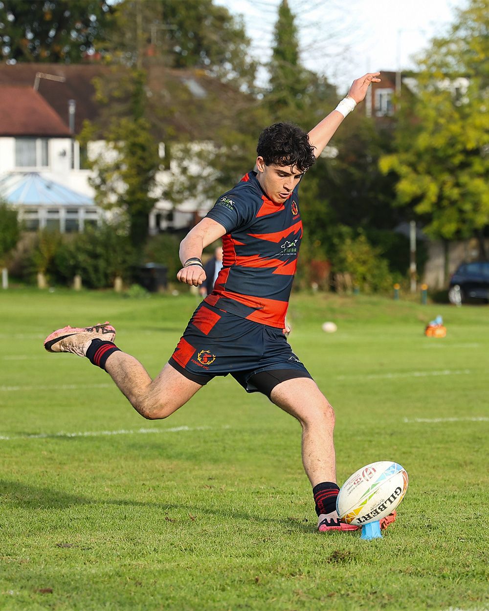 Rugby player kicking the ball during practice on a sunny day.