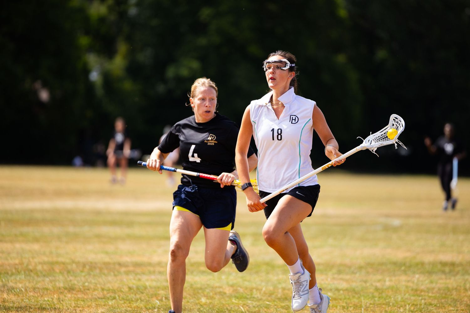 Two ultimate frisbee players compete on a sunny field during a match, with one running to defend against the other.