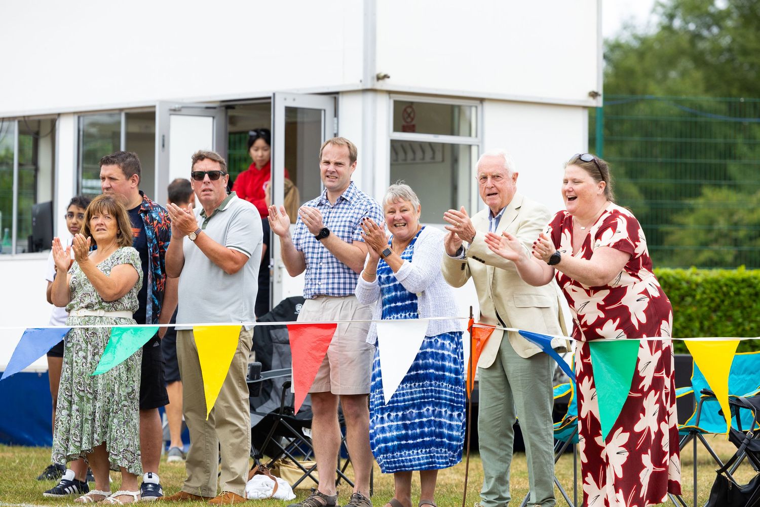 A group of people cheering outdoors at a summer event with colorful bunting decorations in the background.