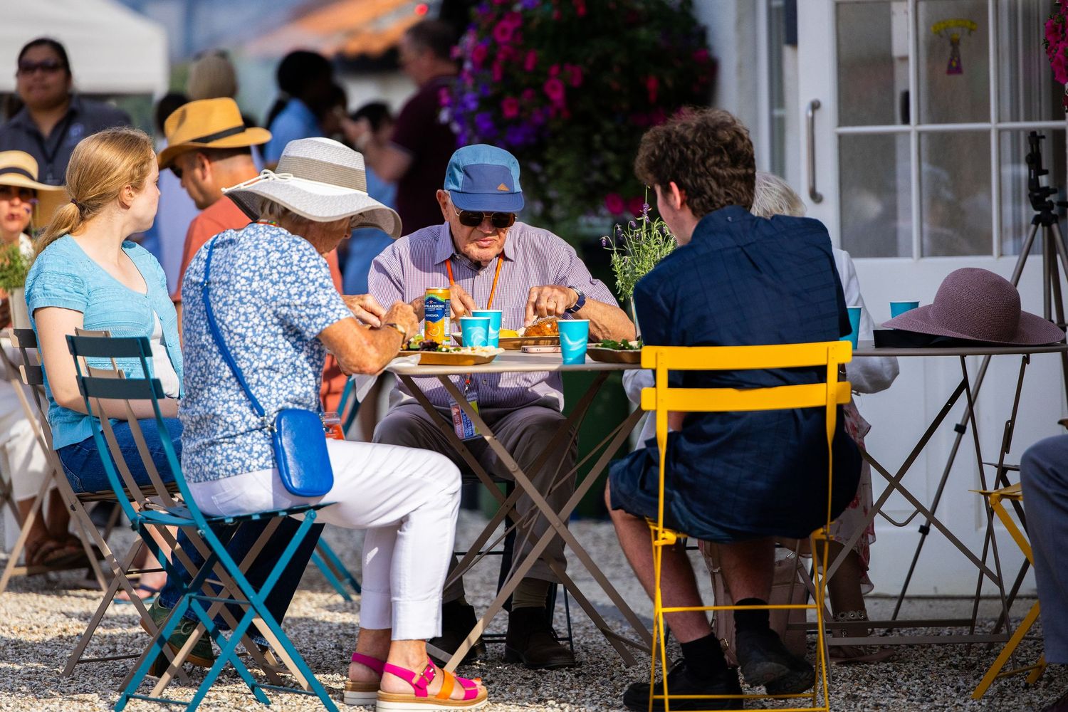 People enjoying a casual outdoor gathering at tables with colorful chairs.