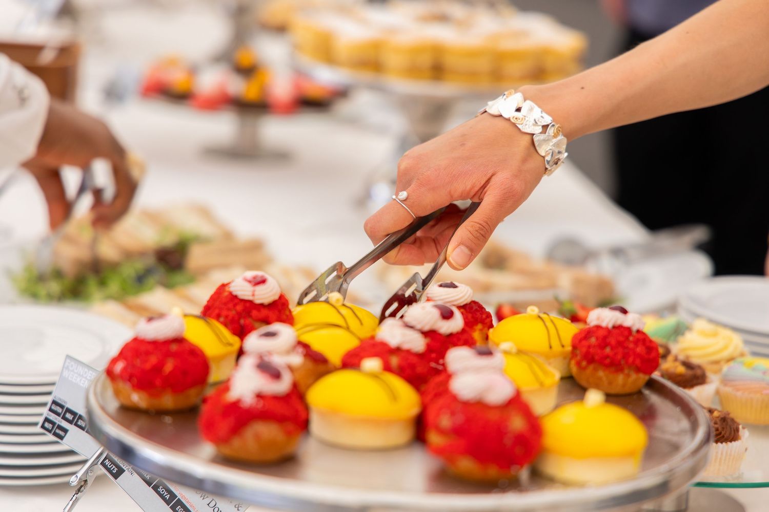 Hand reaching for colorful dessert tarts displayed on serving platter.