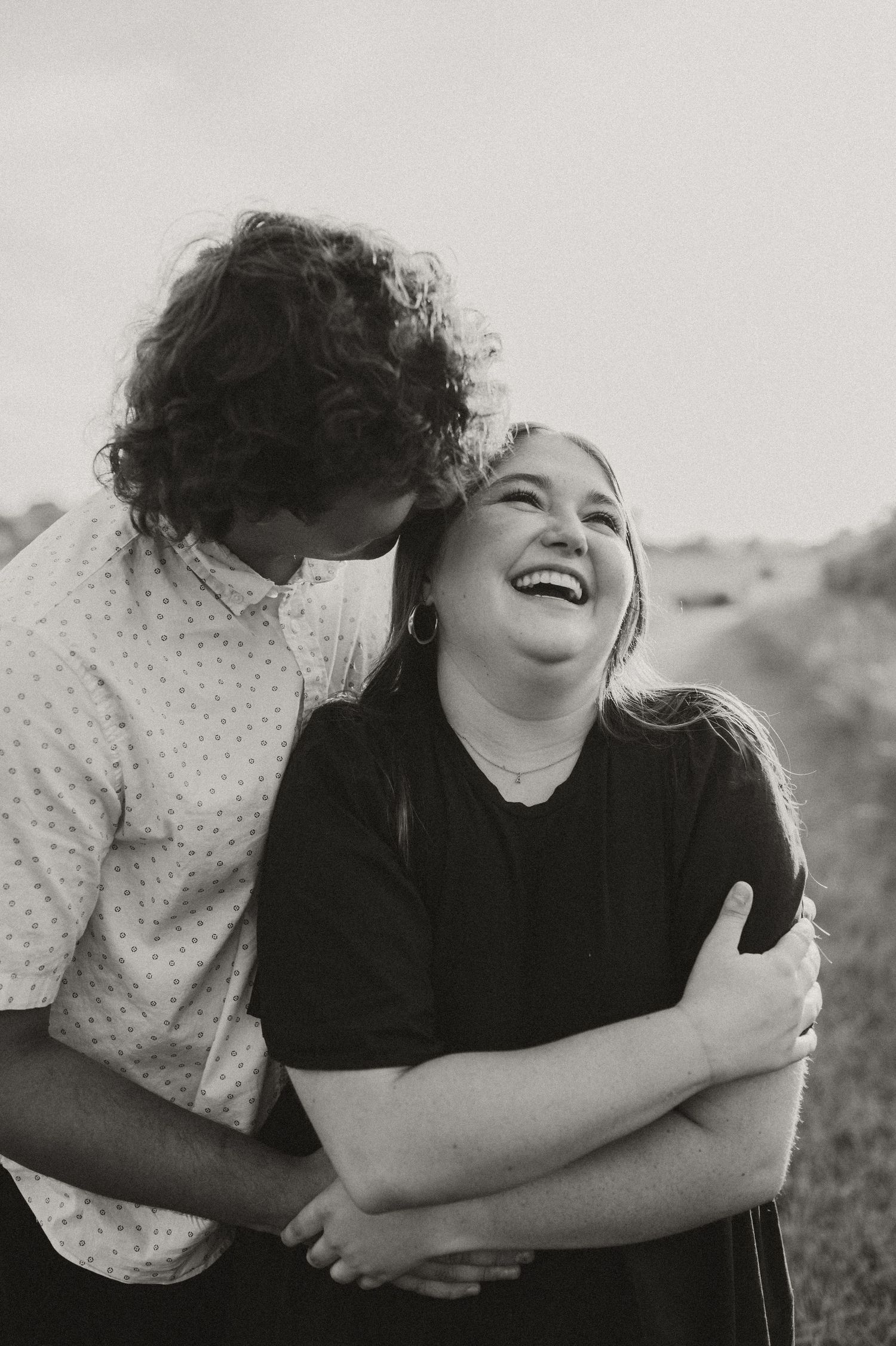 Black and white photo series showing joyful candid moments of embracing and laughter in an outdoor setting.