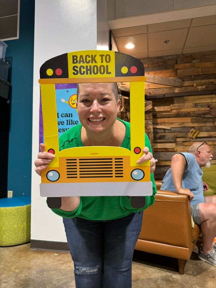 A person holds up a yellow school bus photo prop frame with 'Back to School' text at an indoor event.