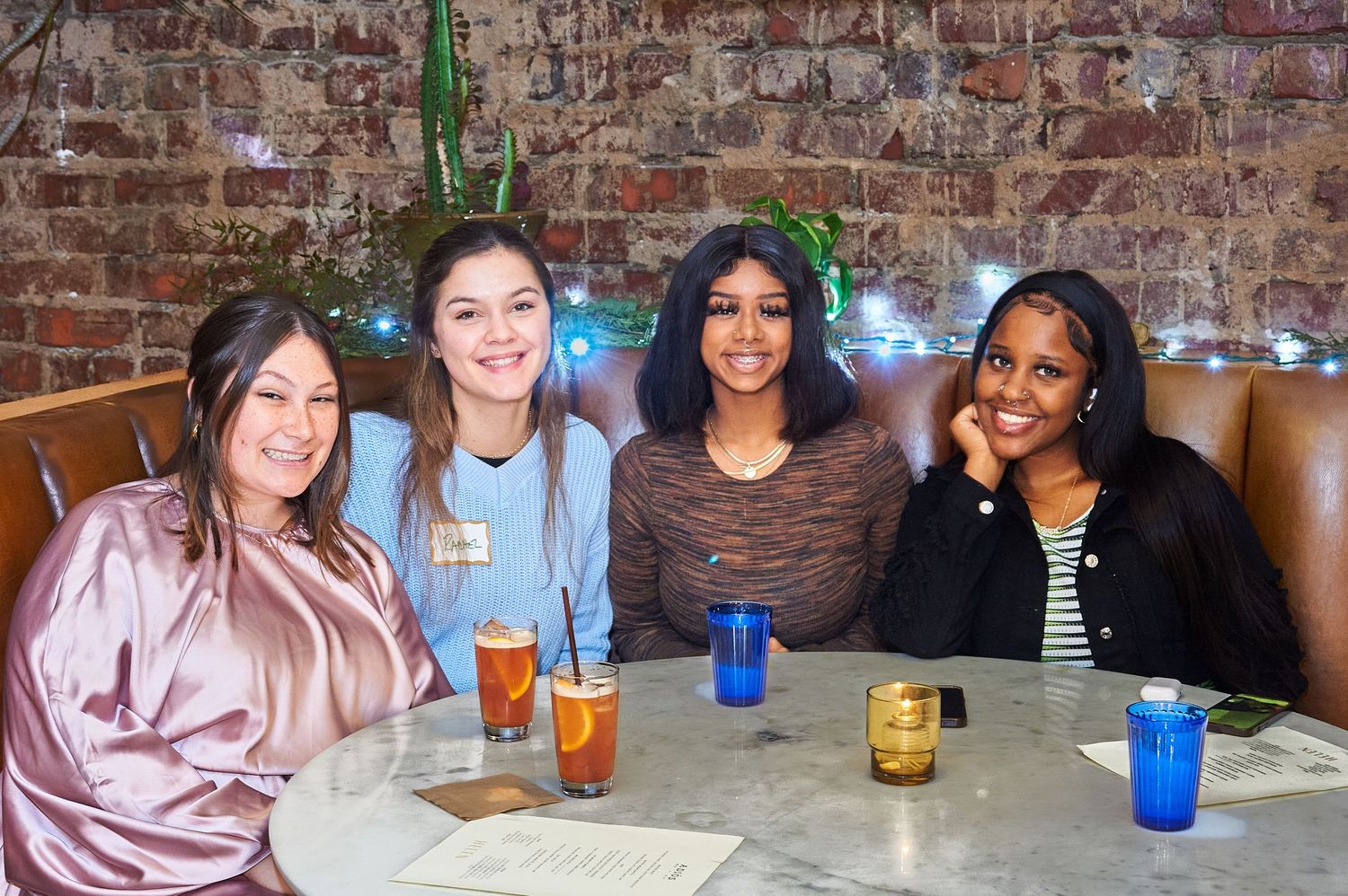 Group of friends enjoying drinks together at a restaurant with brick wall background.