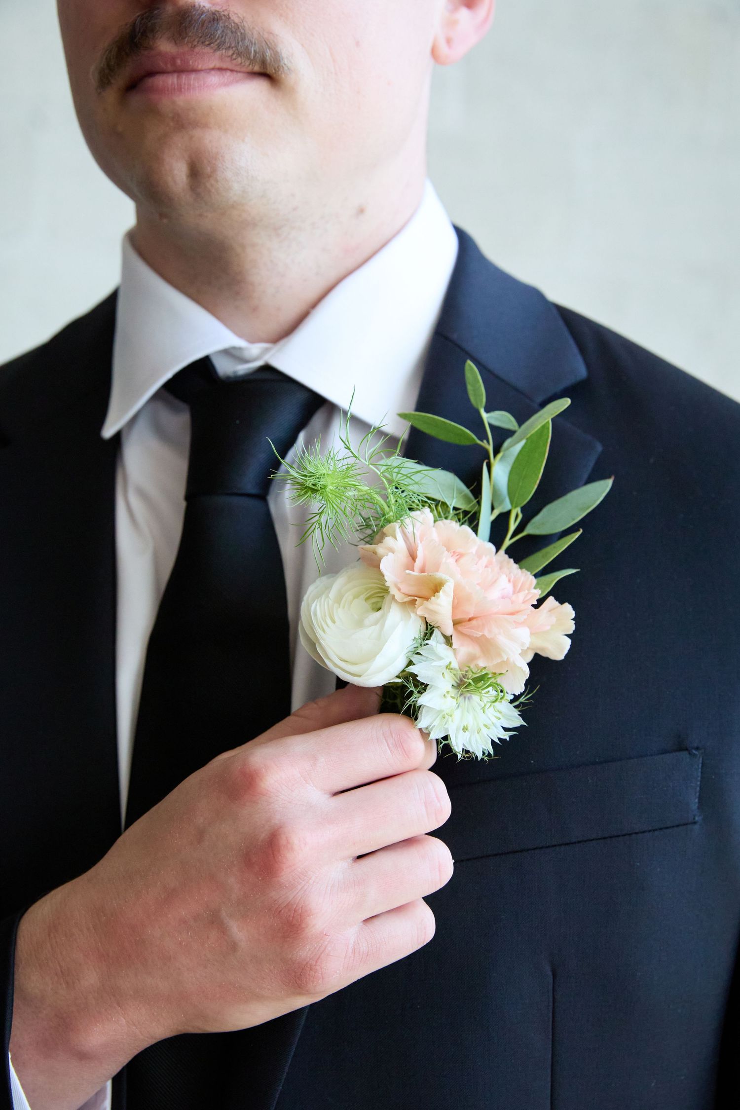 Close-up of groom's boutonniere with pink and white flowers on black suit lapel.