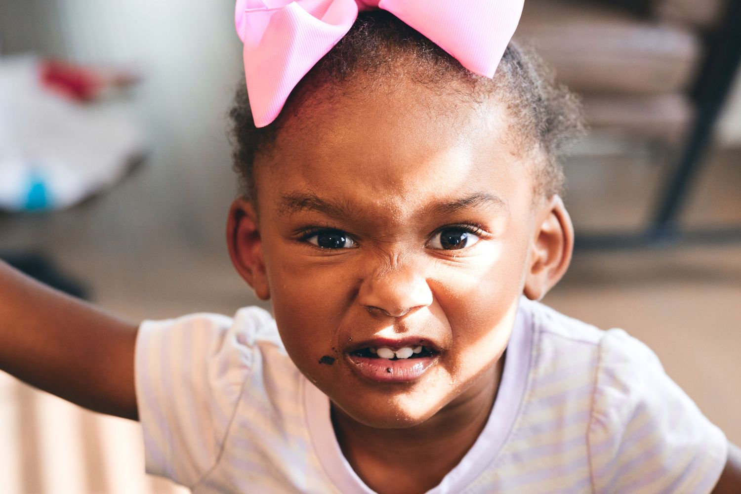 Young child wearing pink bow smiling in natural lighting.