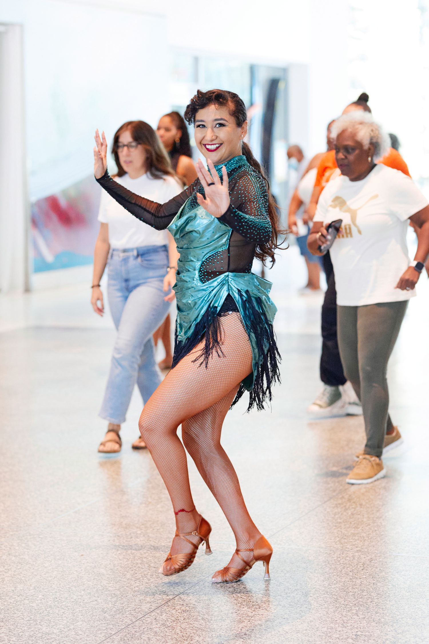 People participating in dance class with dancer in teal fringe dress.