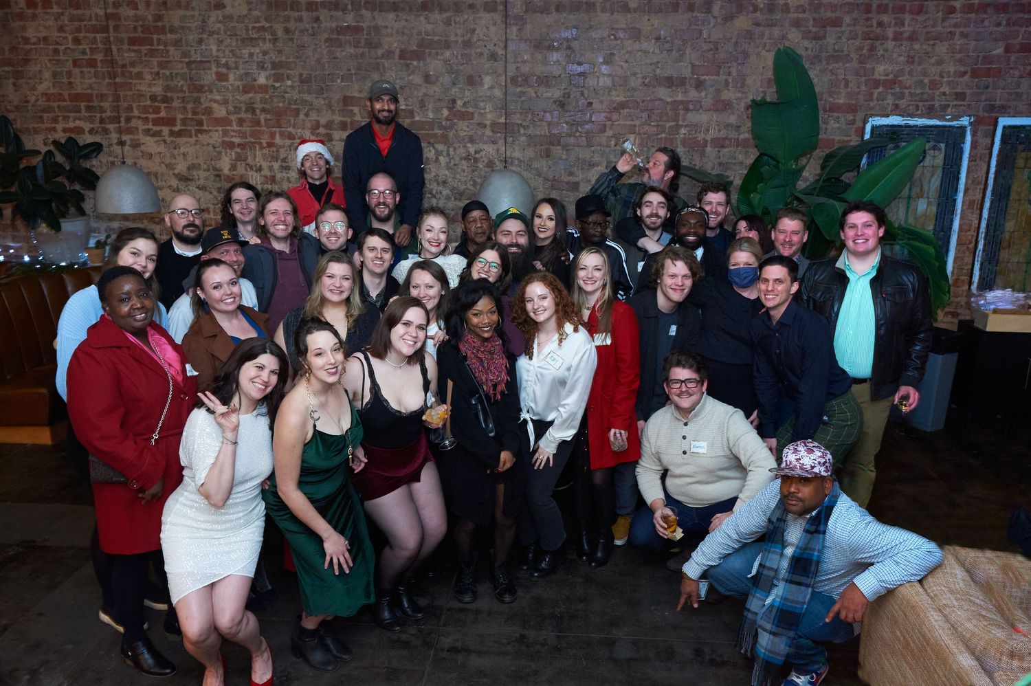 Group celebration photo with crowd posing together against industrial brick wall background.