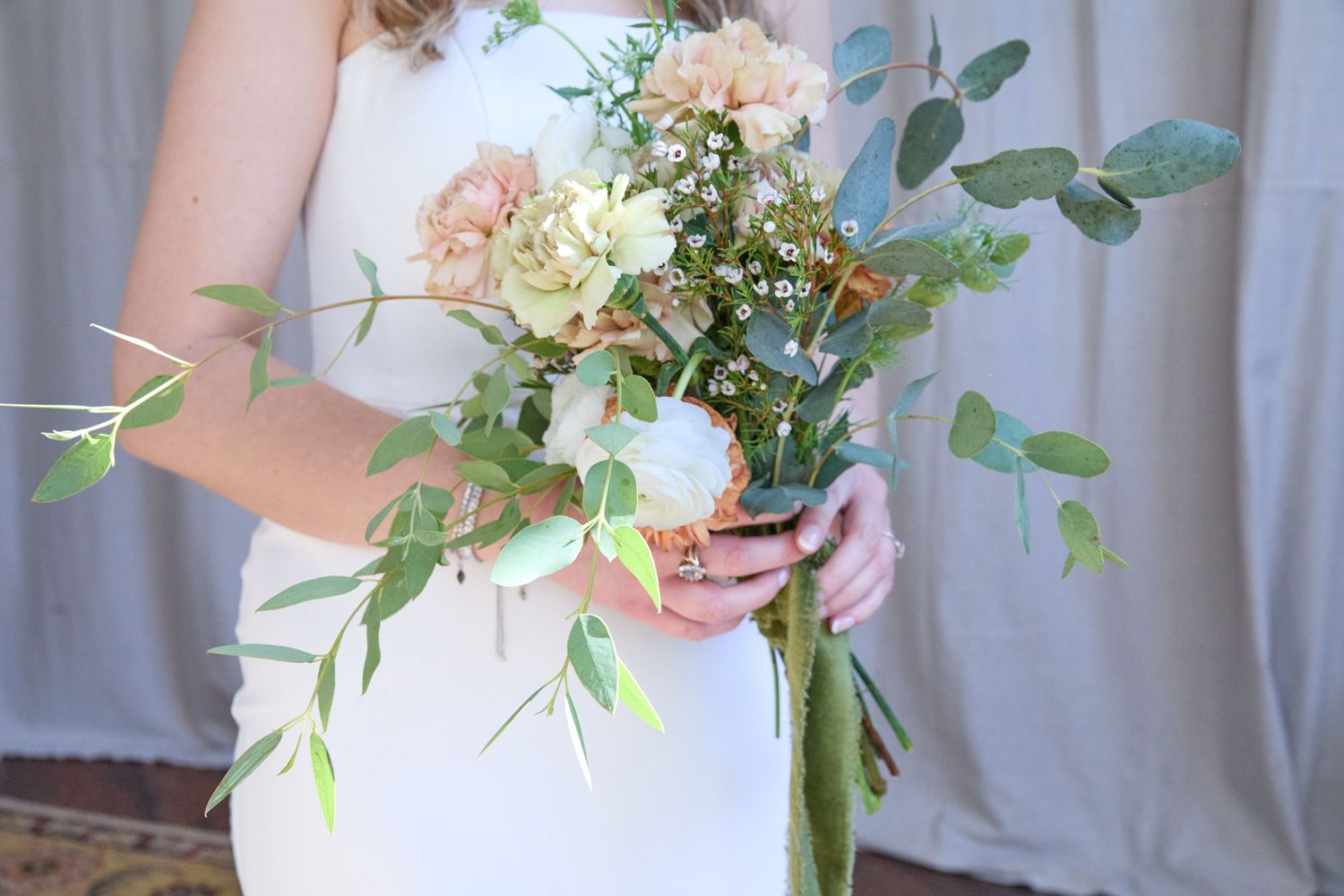 A delicate bridal bouquet with peach flowers, white blooms and fresh eucalyptus greenery.