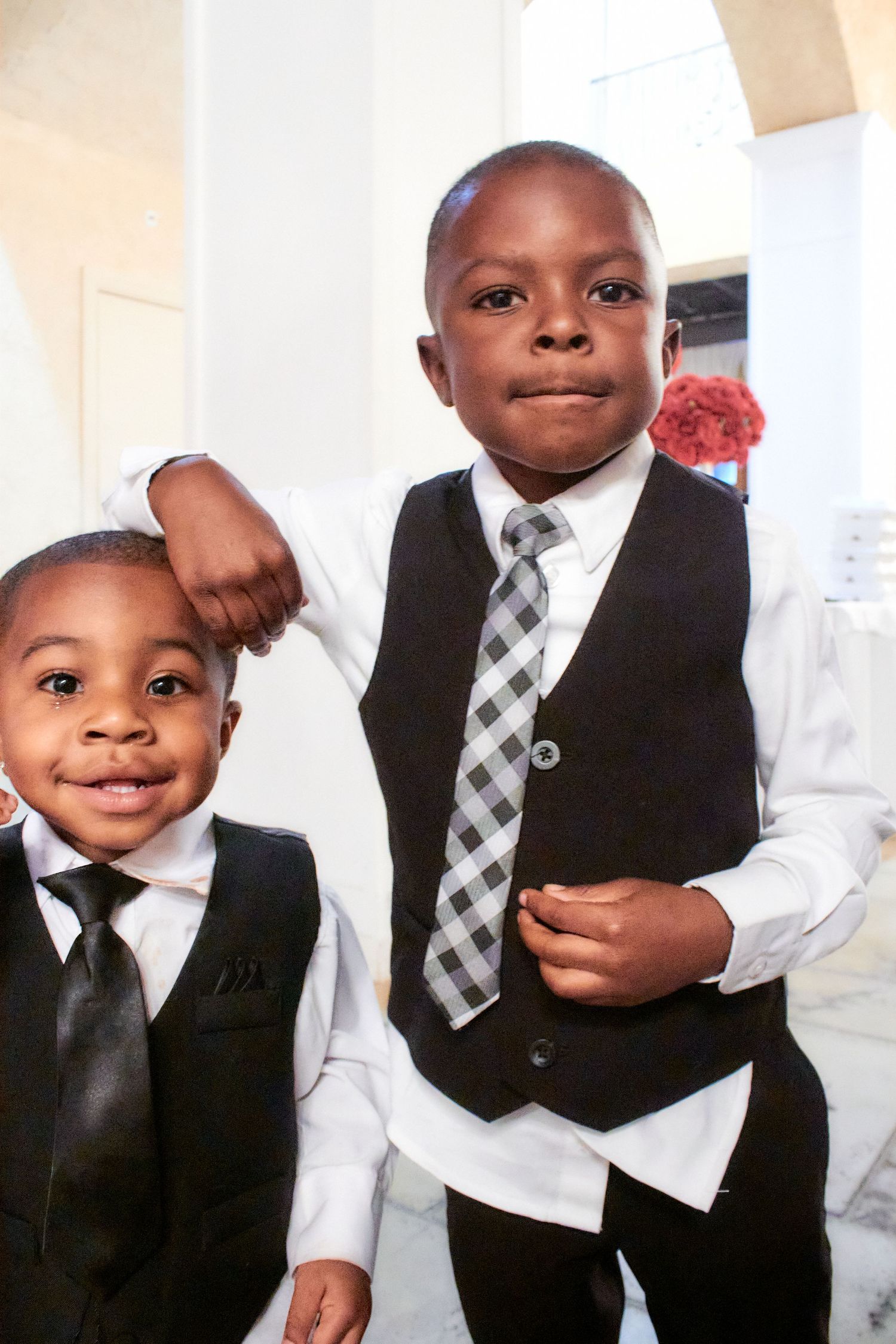 Two young boys dressed in formal black suits and ties posing together.