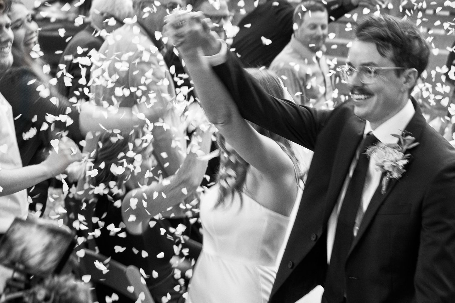 A joyful wedding celebration with confetti flying through the air in black and white.