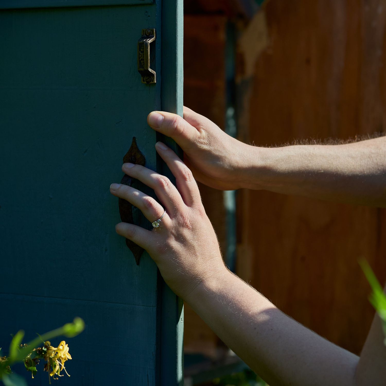 Hands installing or adjusting hardware on dark green surface in natural lighting.