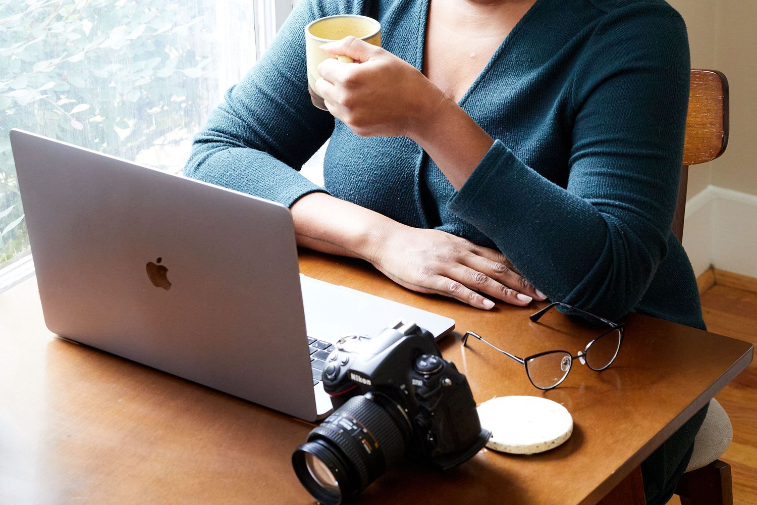 Person working at desk with MacBook laptop, camera, and coffee.