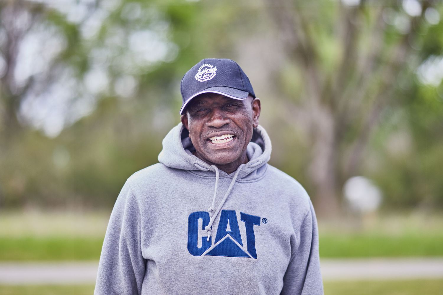 Person wearing a grey CAT hoodie and baseball cap smiling outdoors.