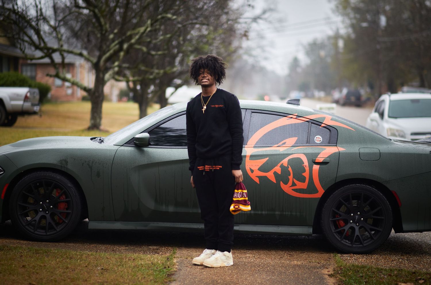 Person standing beside a dark sports car with custom orange graphics.