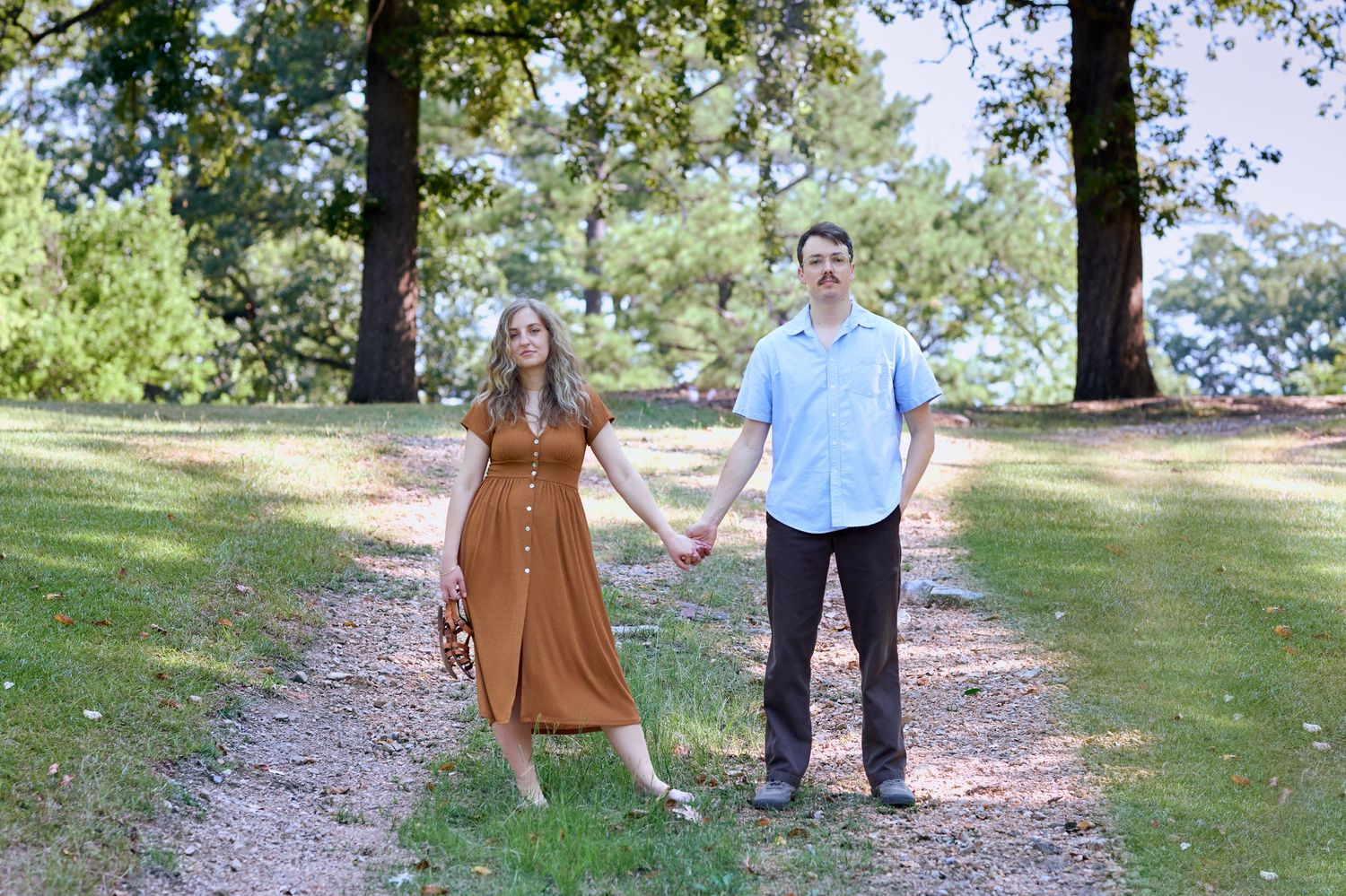 A couple holding hands while standing on a tree-lined path in a park.