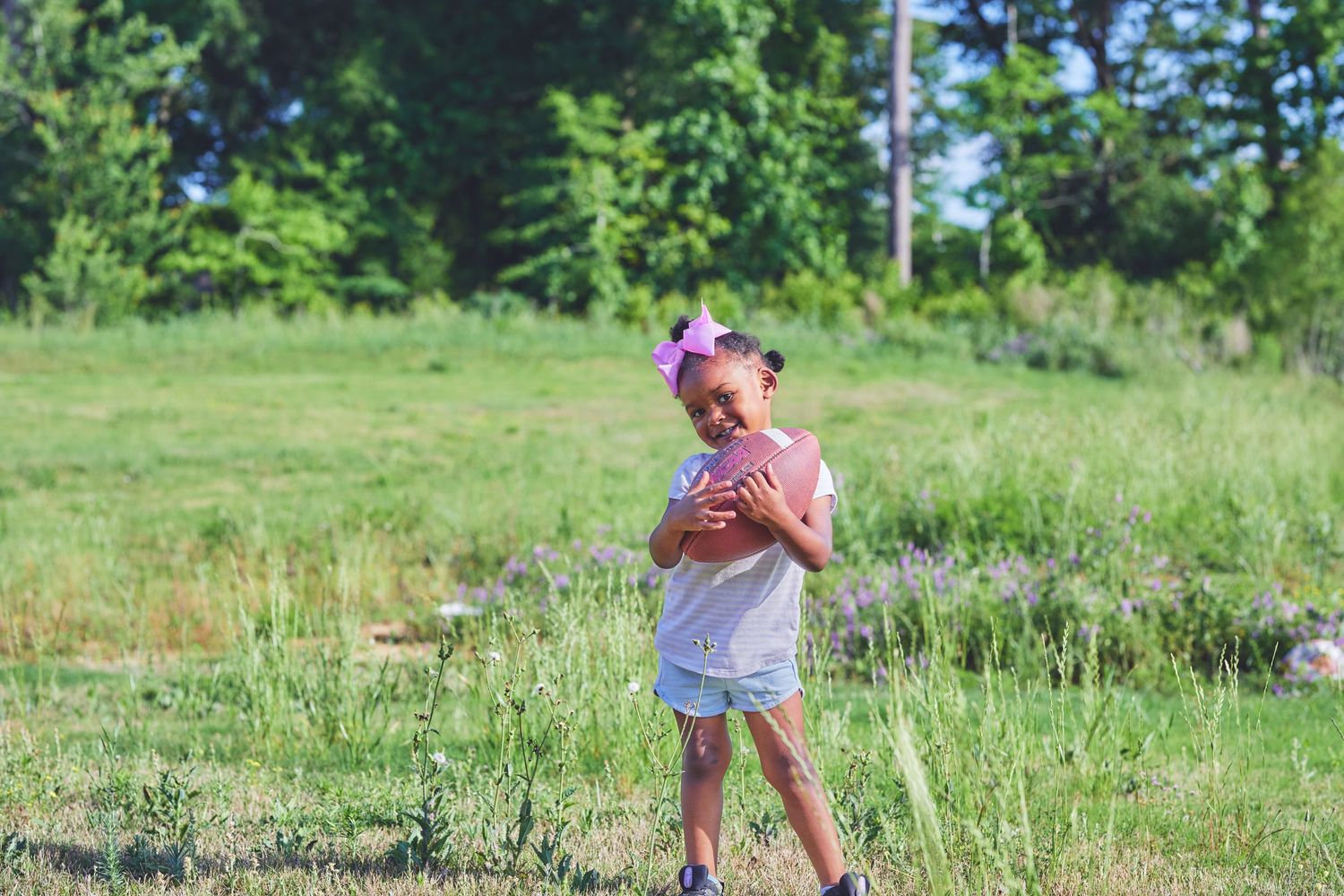 Person in white clothing playing with a football in a sunny green field.