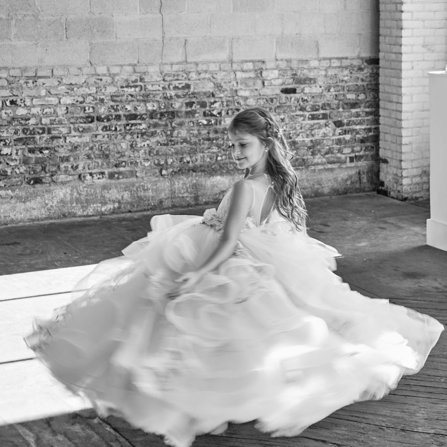 A flowing white wedding dress spins dramatically against a rustic brick wall background.
