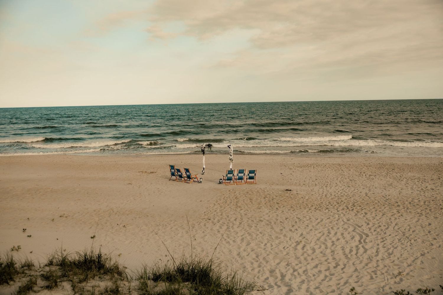 Small beach gathering with chairs arranged on sandy shore near calm ocean waves under overcast sky at topsail beach, NC.