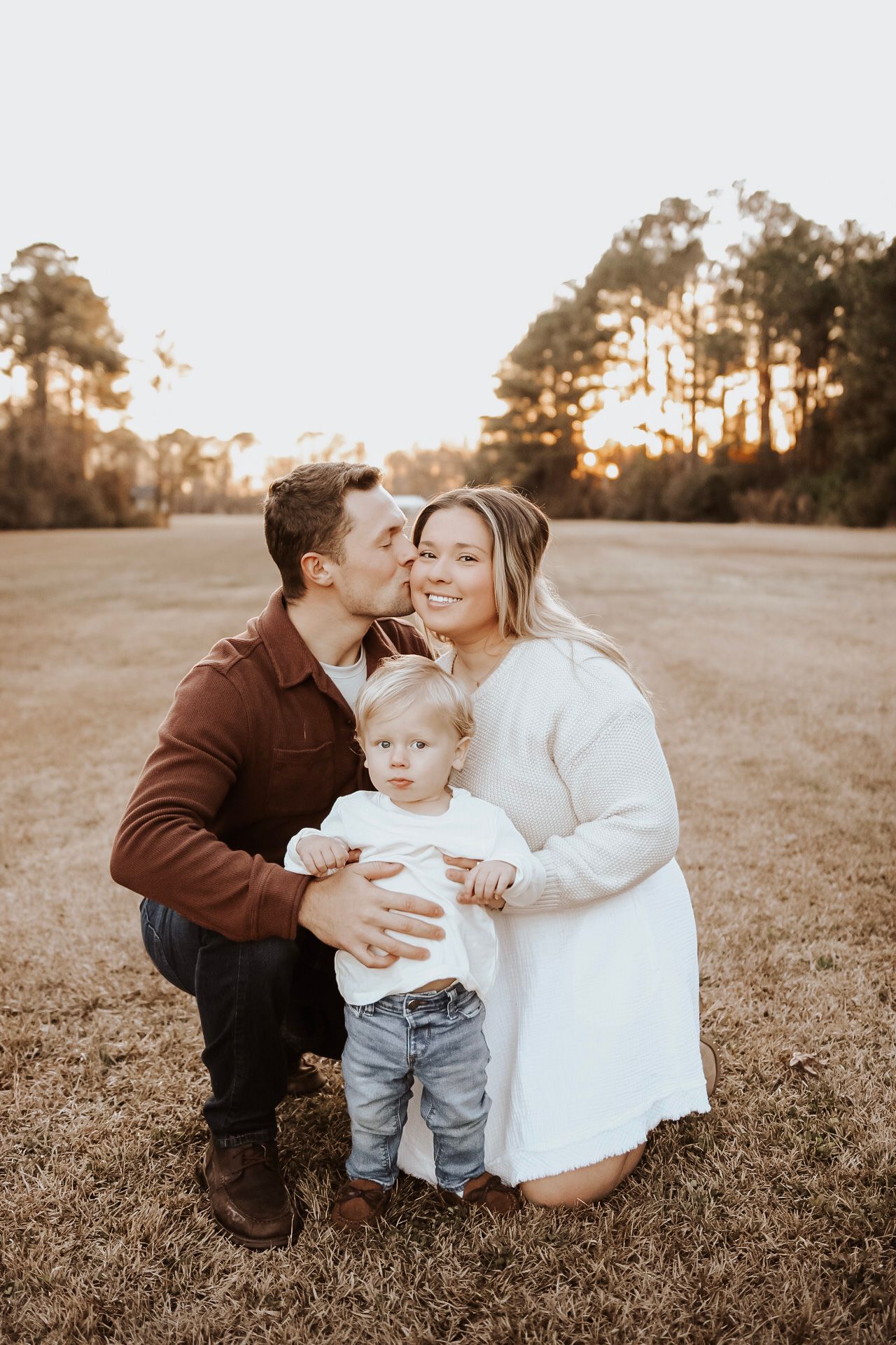 Family shares tender moments together on grassy field at sunset.
