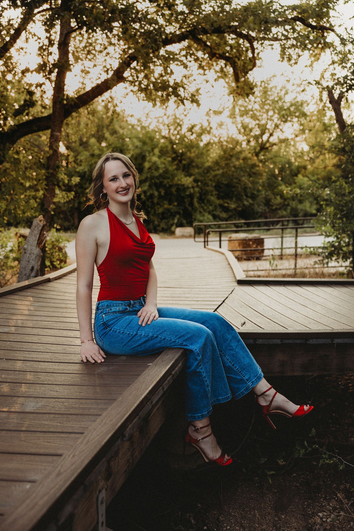 High school senior seated on a wooden boardwalk surrounded by mature trees during an outdoor senior portrait session in Abilene, Texas.