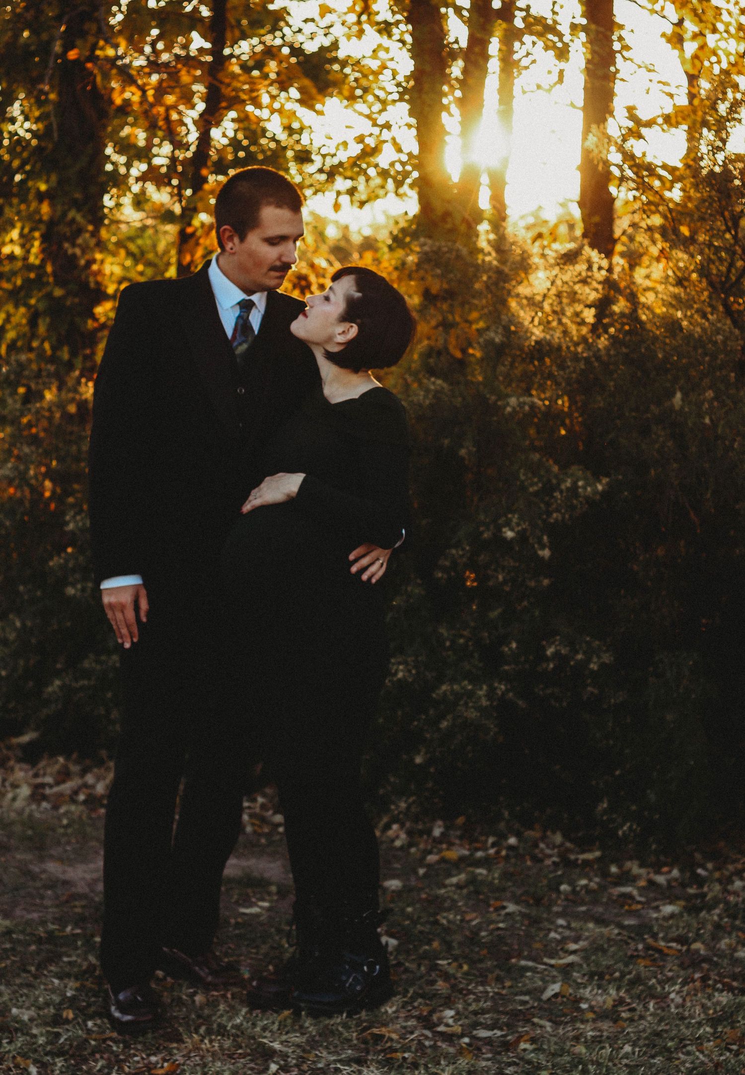 Couple in black formal wear sharing a romantic moment in a golden sunset forest setting in Abilene Texas
