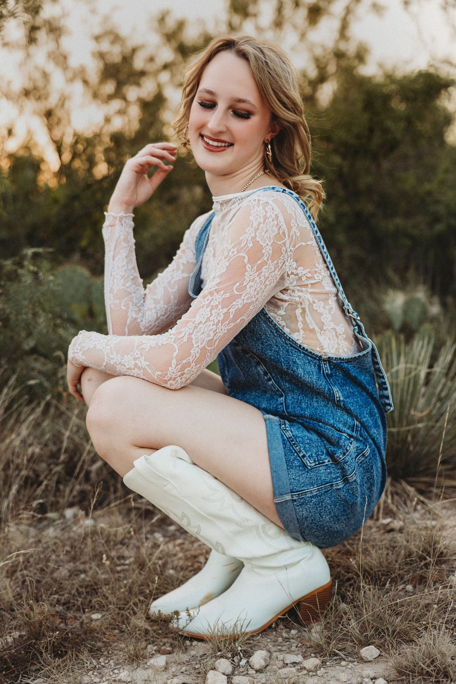 High school senior smiling while crouched in a natural field during a golden hour senior photography session in Abilene, Texas.