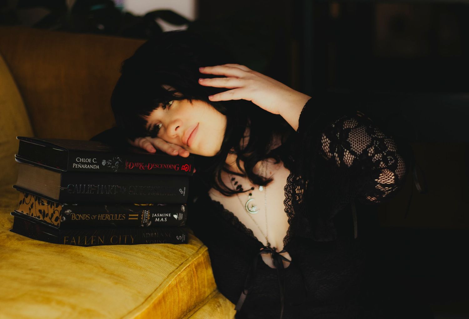 Cinematic creative portrait session in Abilene TX featuring a subject reclining on a couch surrounded by books with soft, moody lighting