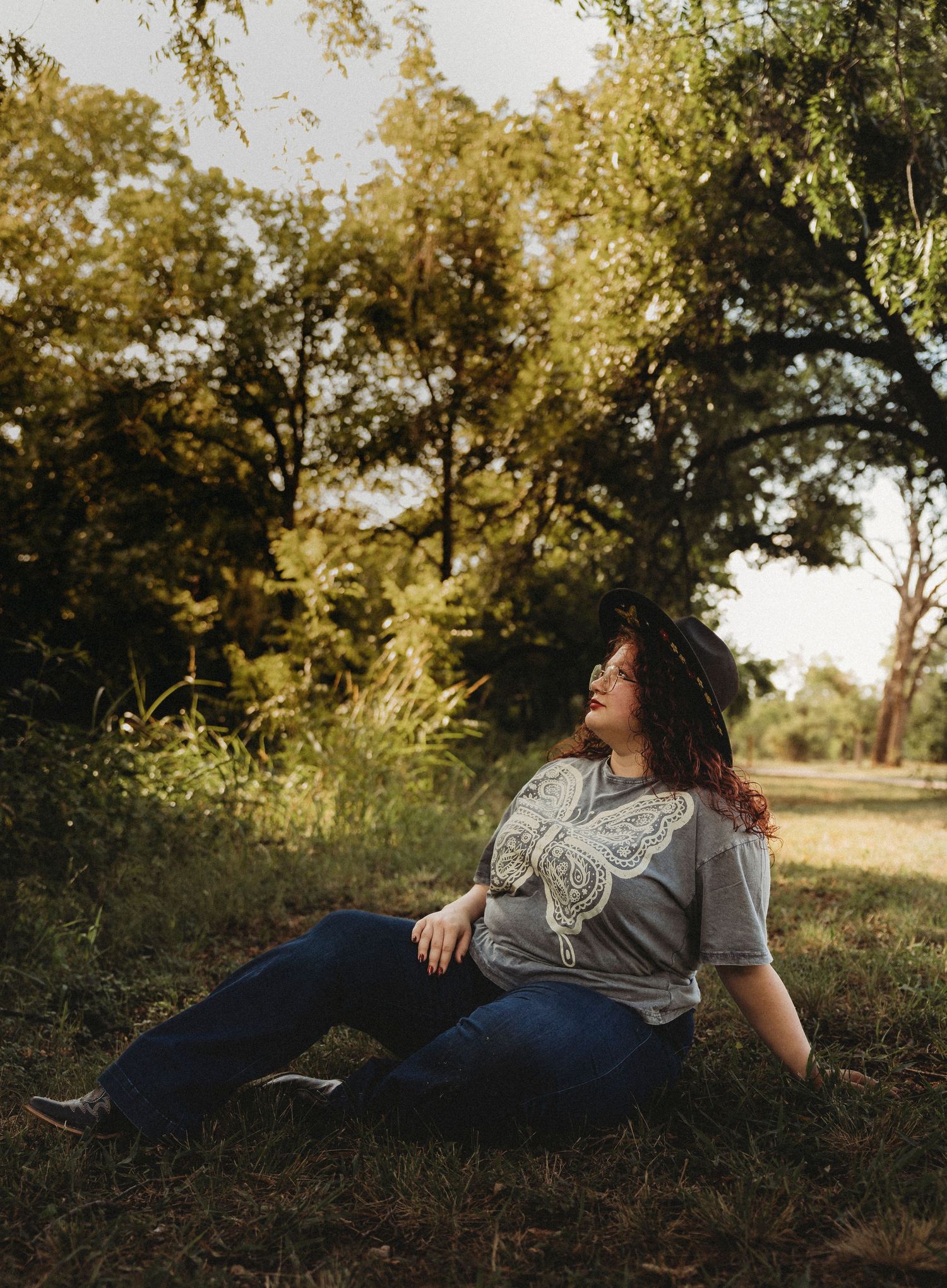 Outdoor senior portrait of a Jim Ned High School senior sitting in the grass surrounded by warm golden light during a senior session