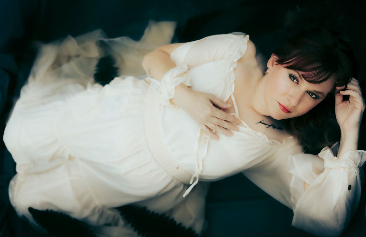 Moody portrait of a woman in a white gown floating on dark water with soft, ethereal movement