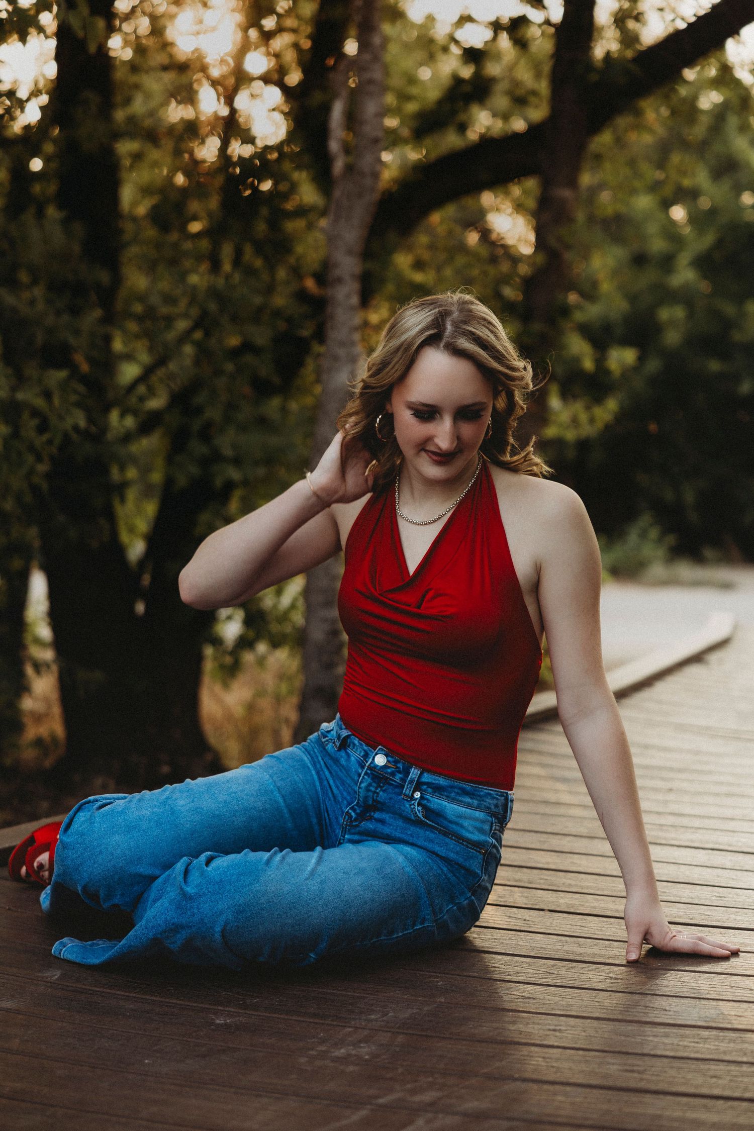 High school senior in a red top and jeans posing on a wooden boardwalk during a golden hour senior portrait session in Abilene, Texas.
