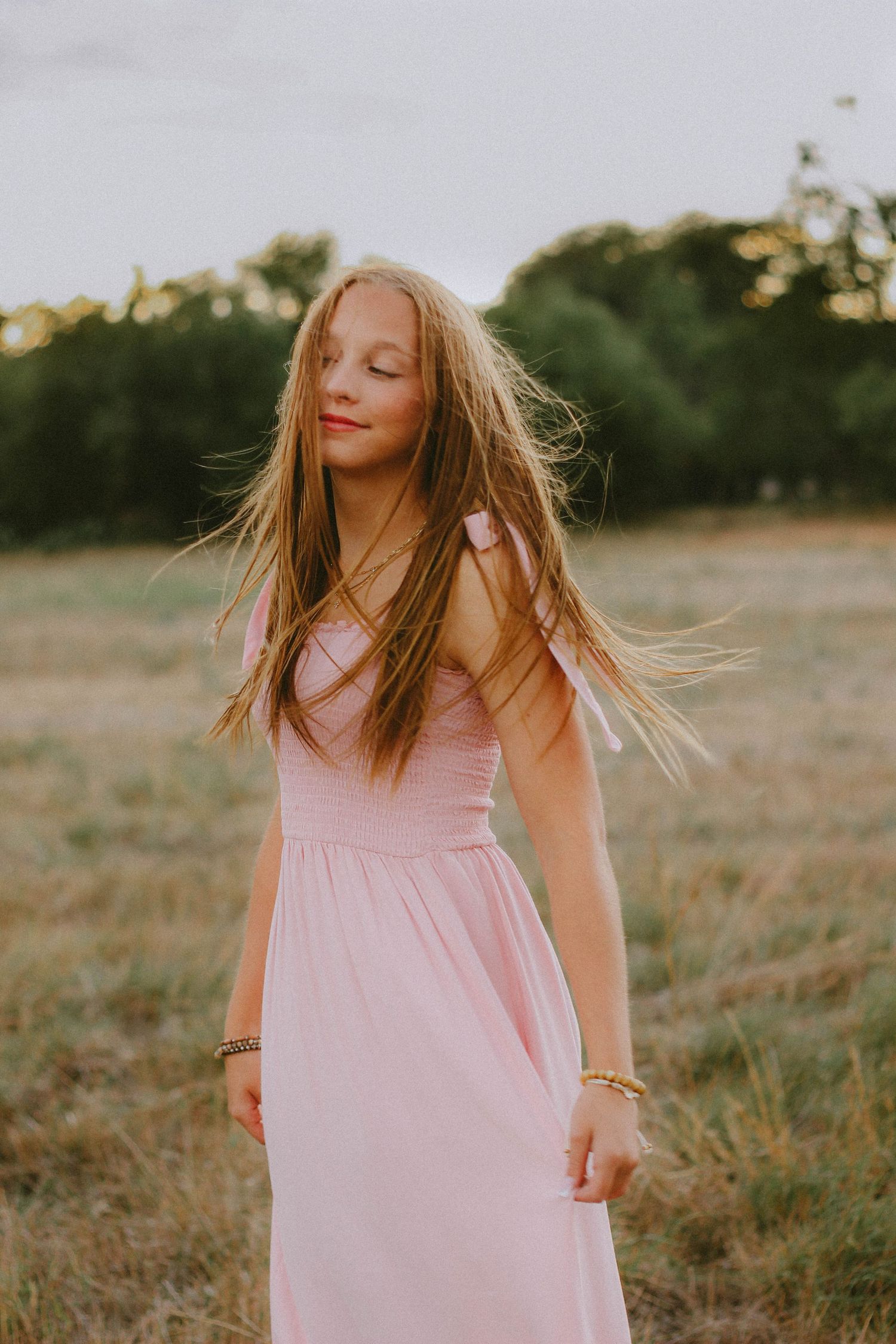 Senior girl in a flowing pink dress standing in an open field during a golden hour senior photography session in Abilene, Texas.