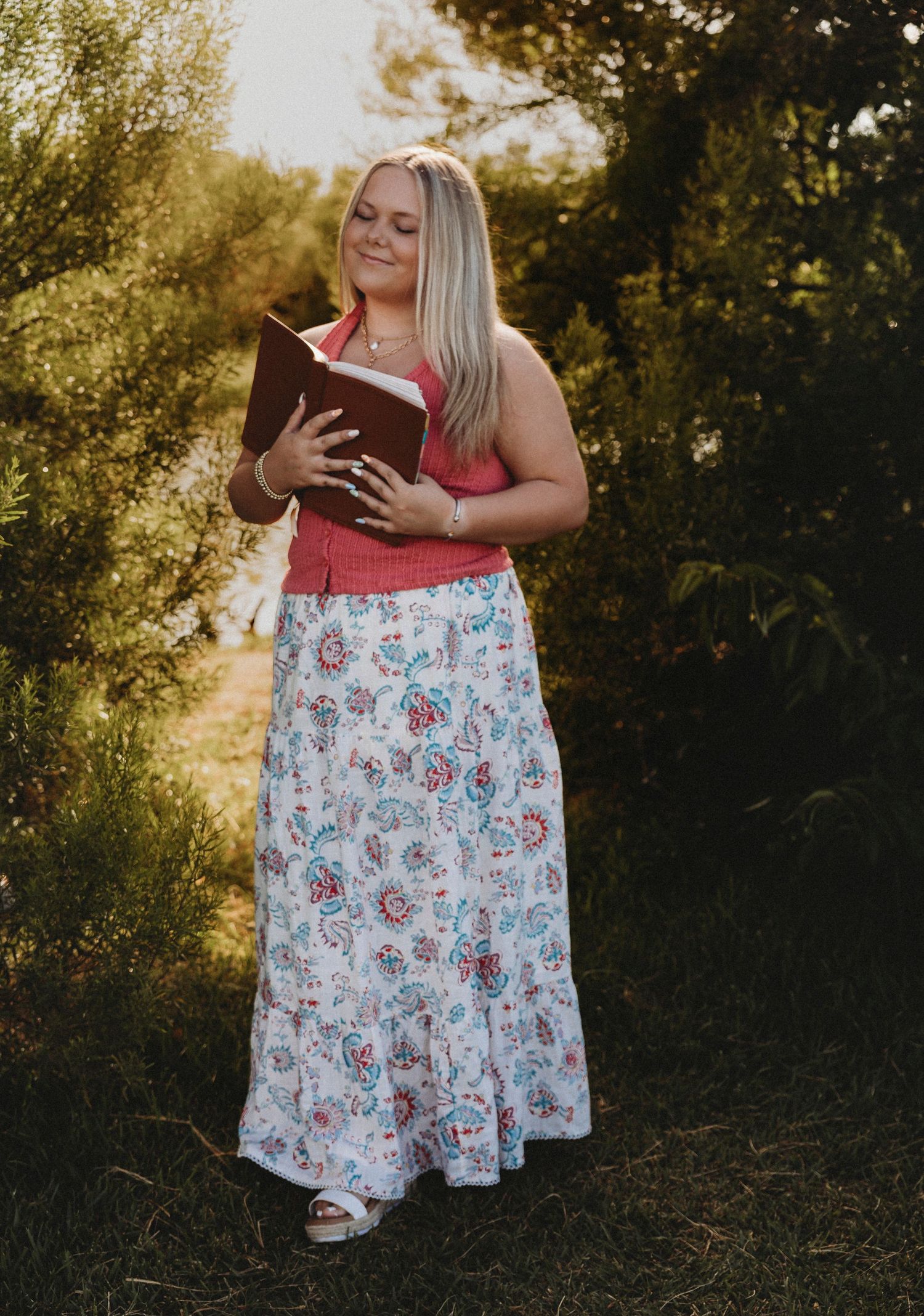 Golden hour senior portrait of a high school senior in a floral skirt holding bible during an outdoor senior photos session in Abilene, Texa