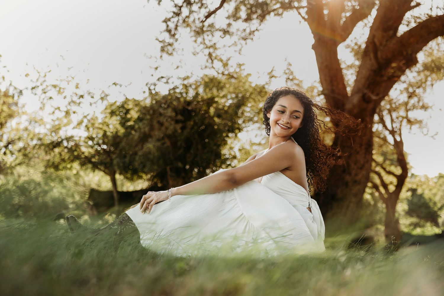 Joyful outdoor senior portrait of a Class of 2027 senior twirling beneath a large tree during a sunset senior session in Abilene, Texas.