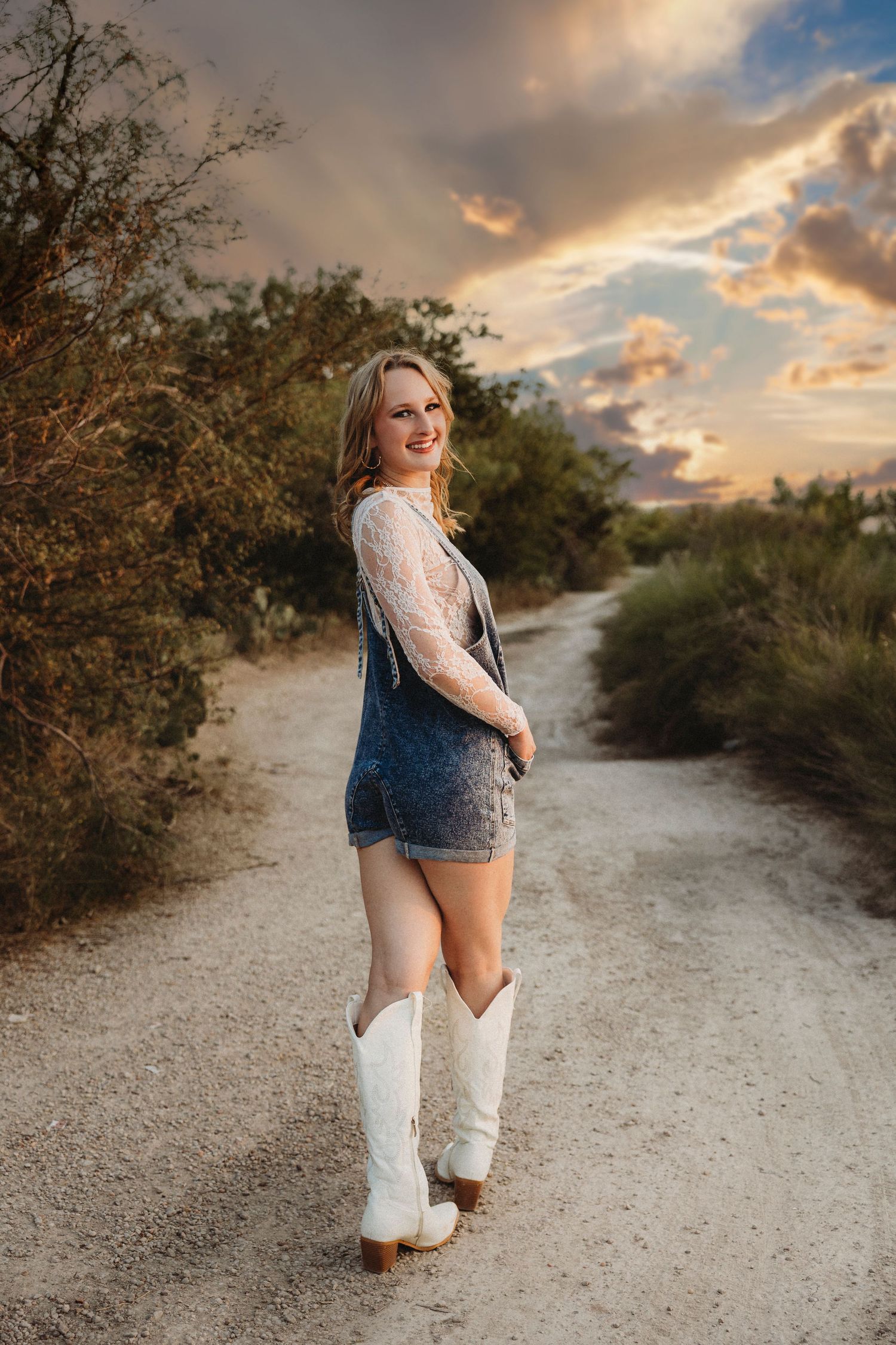 Texas high school senior smiling over her shoulder on a country road during a sunset senior photography session in Abilene.