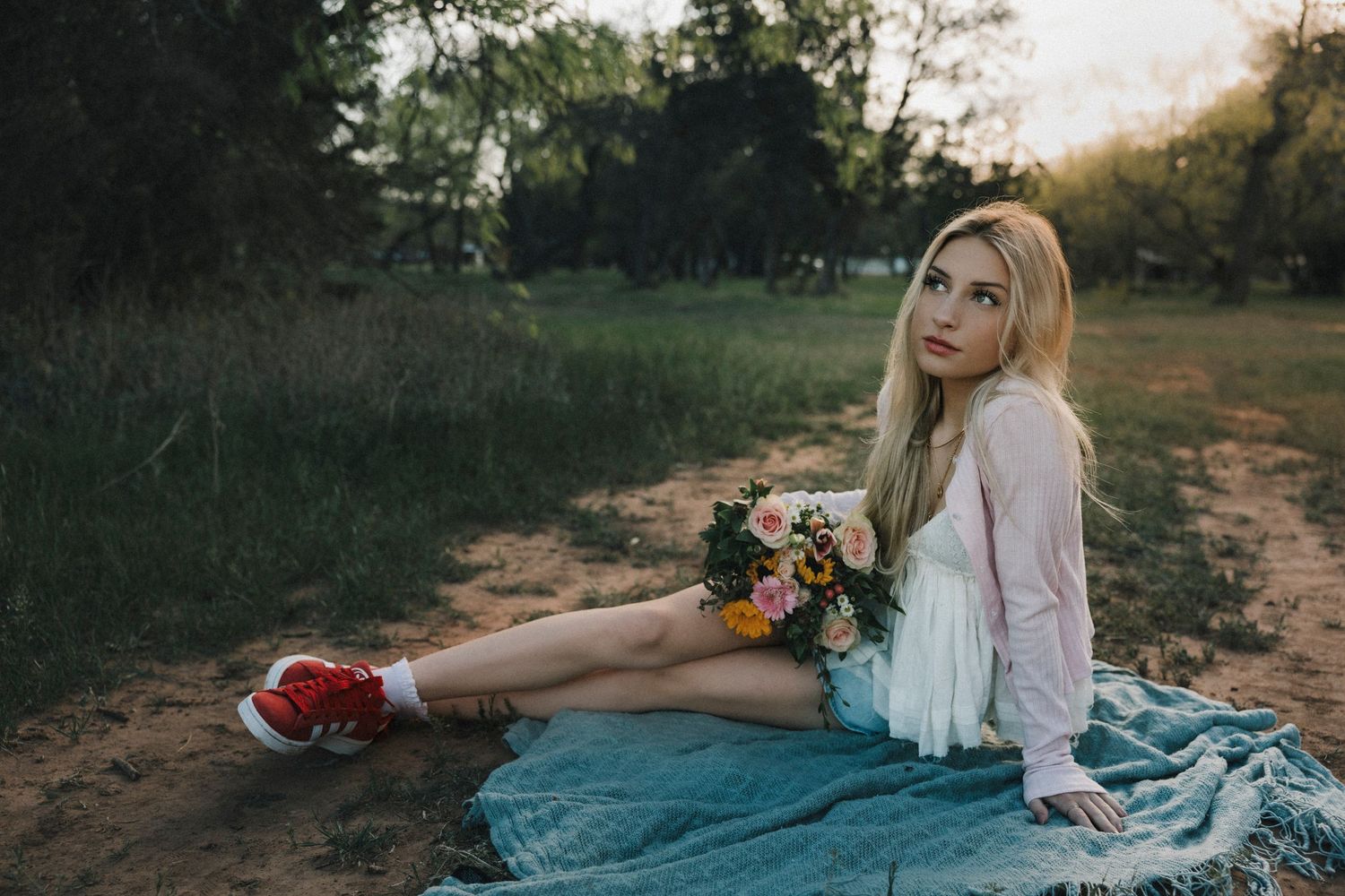 High school senior sitting on a dirt path with sunflowers during a personalized senior photo session in Abilene, Texas