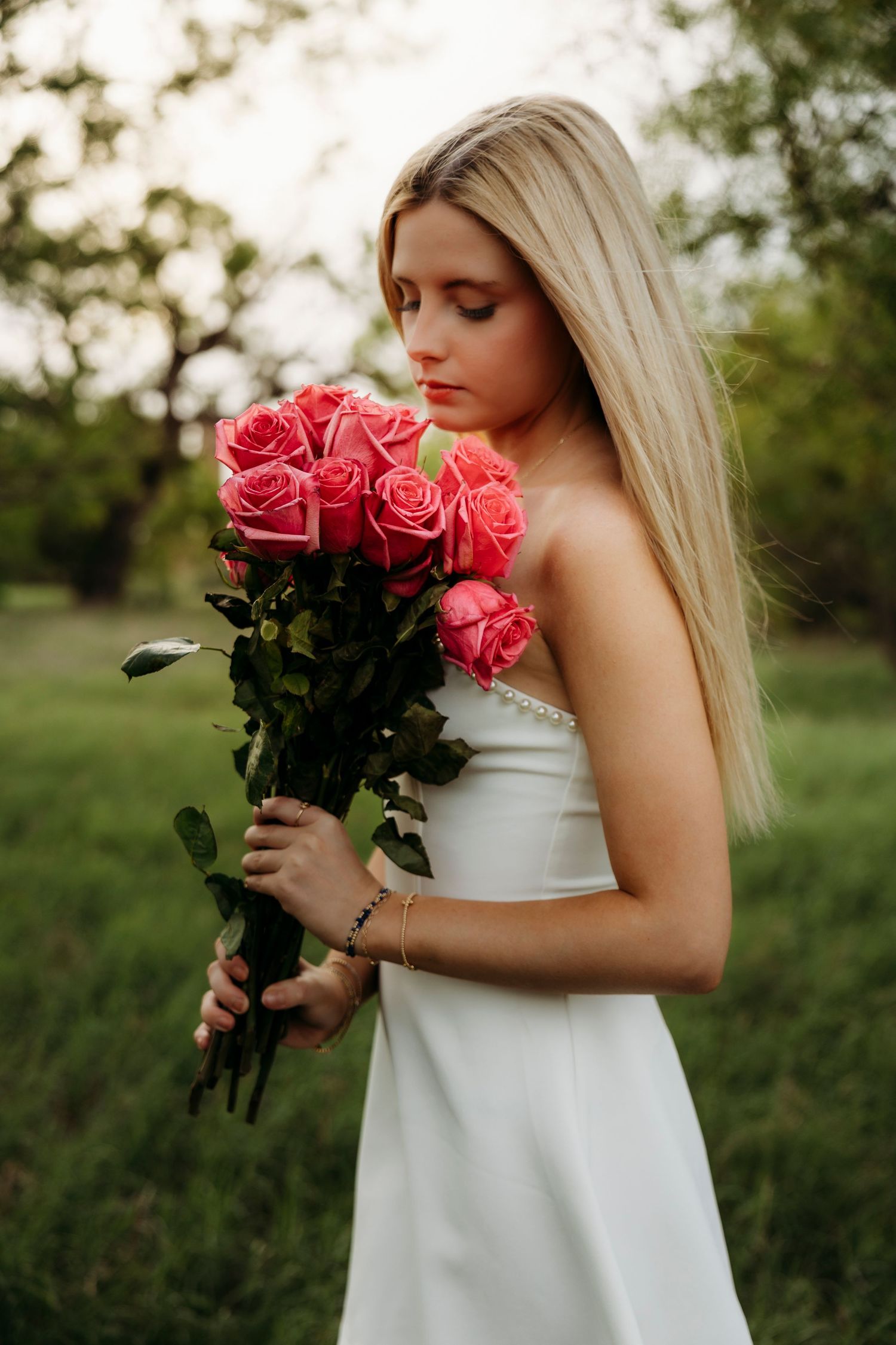 High school senior girl holding pink flowers in a white dress during outdoor senior session in Abilene TX