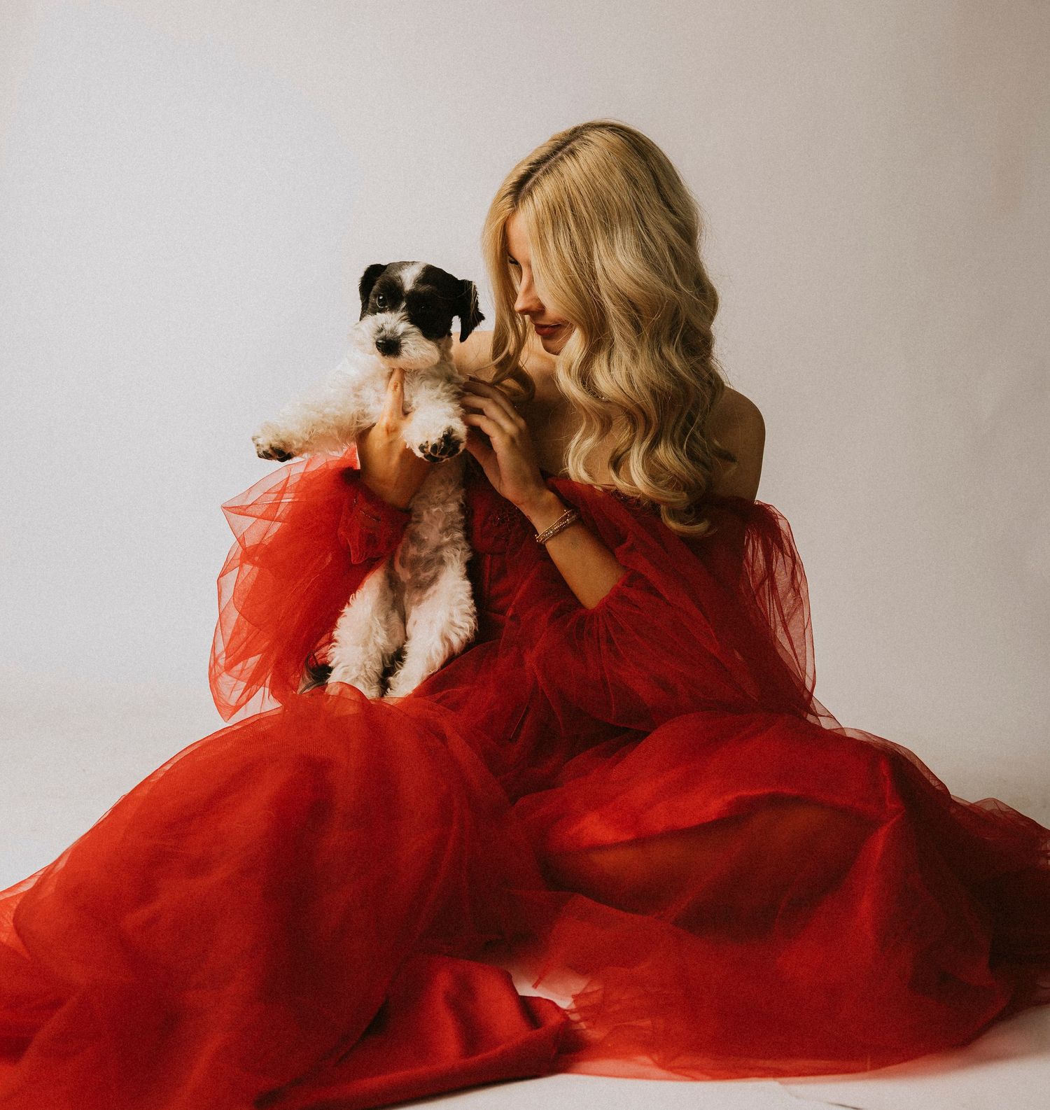 Abilene High School Senior red tulle gown sitting on floor holding a small black and white puppy in a bright studio.