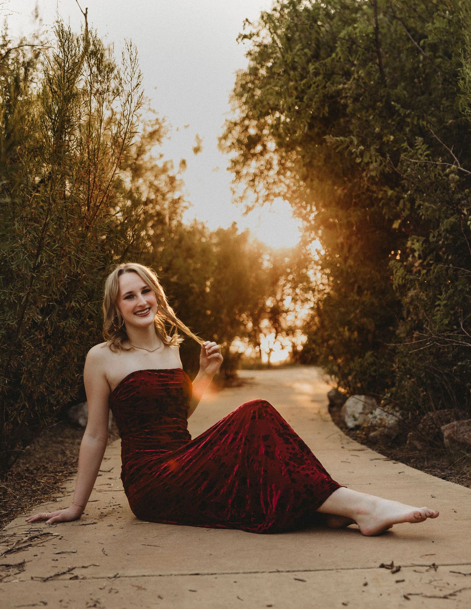 Class of 2027 senior sitting on a quiet pathway beneath glowing sunset light during a cinematic outdoor senior session in Abilene, Texas