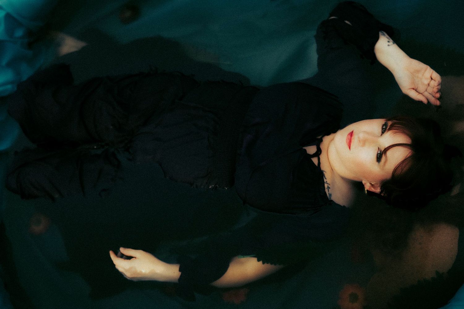 Woman in a black dress floating peacefully in dark water during a cinematic fine art photography session.