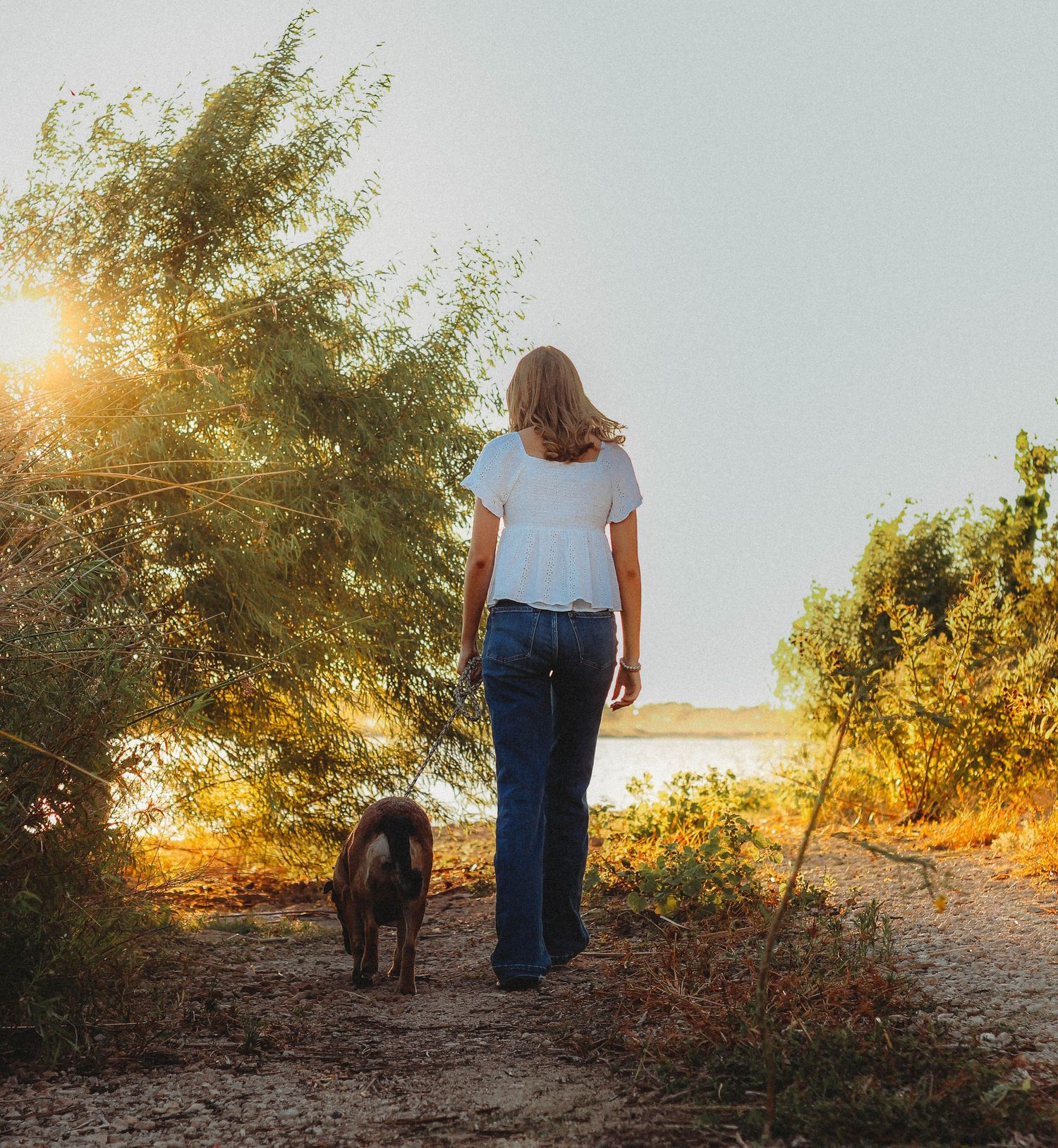 Lifestyle senior portrait session in Abilene TX showing a high school senior walking at sunset with her dog