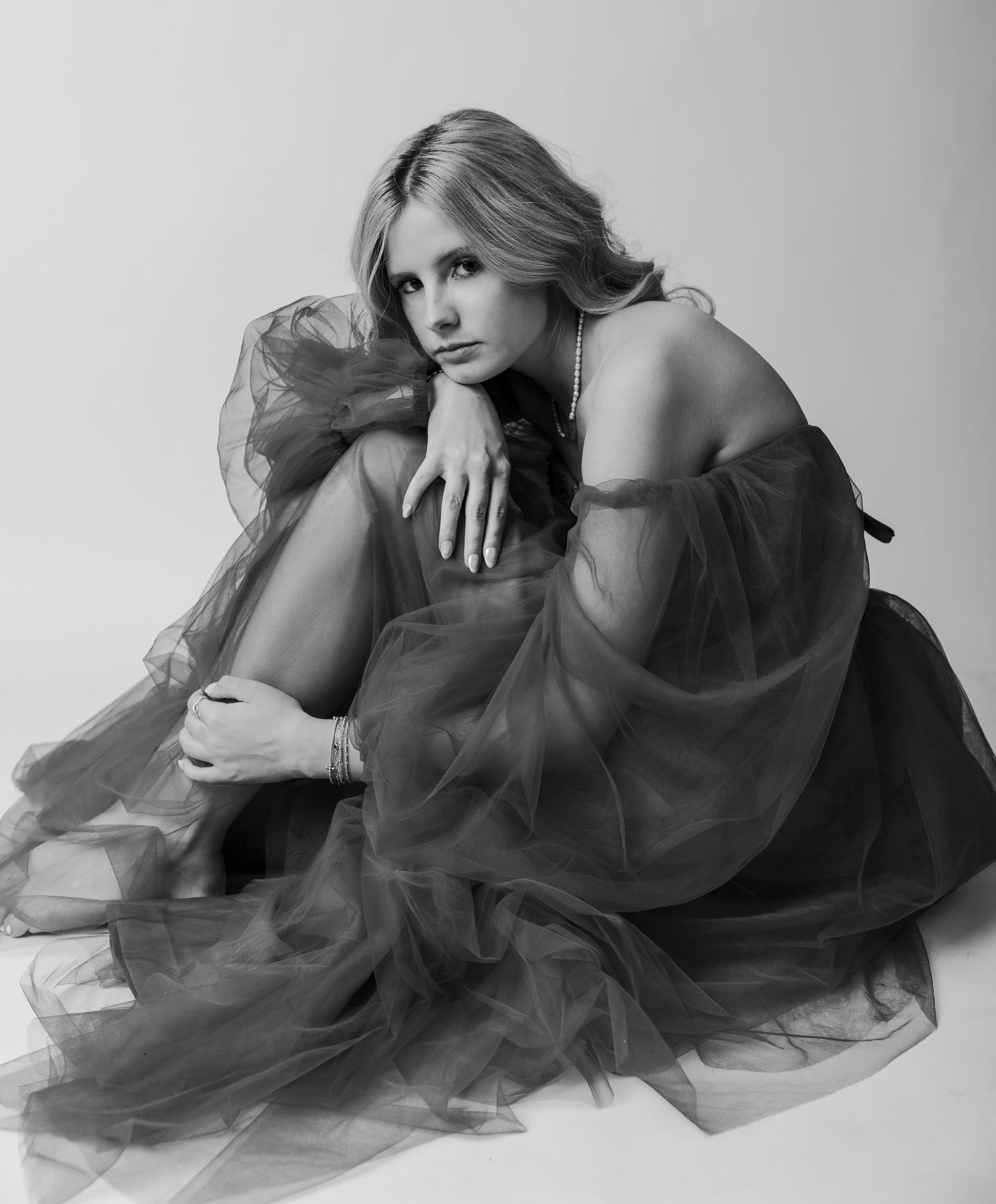 Black and white photo of a Abilene TX High School Senior in a flowing tulle gown sitting gracefully on the floor in a studio.