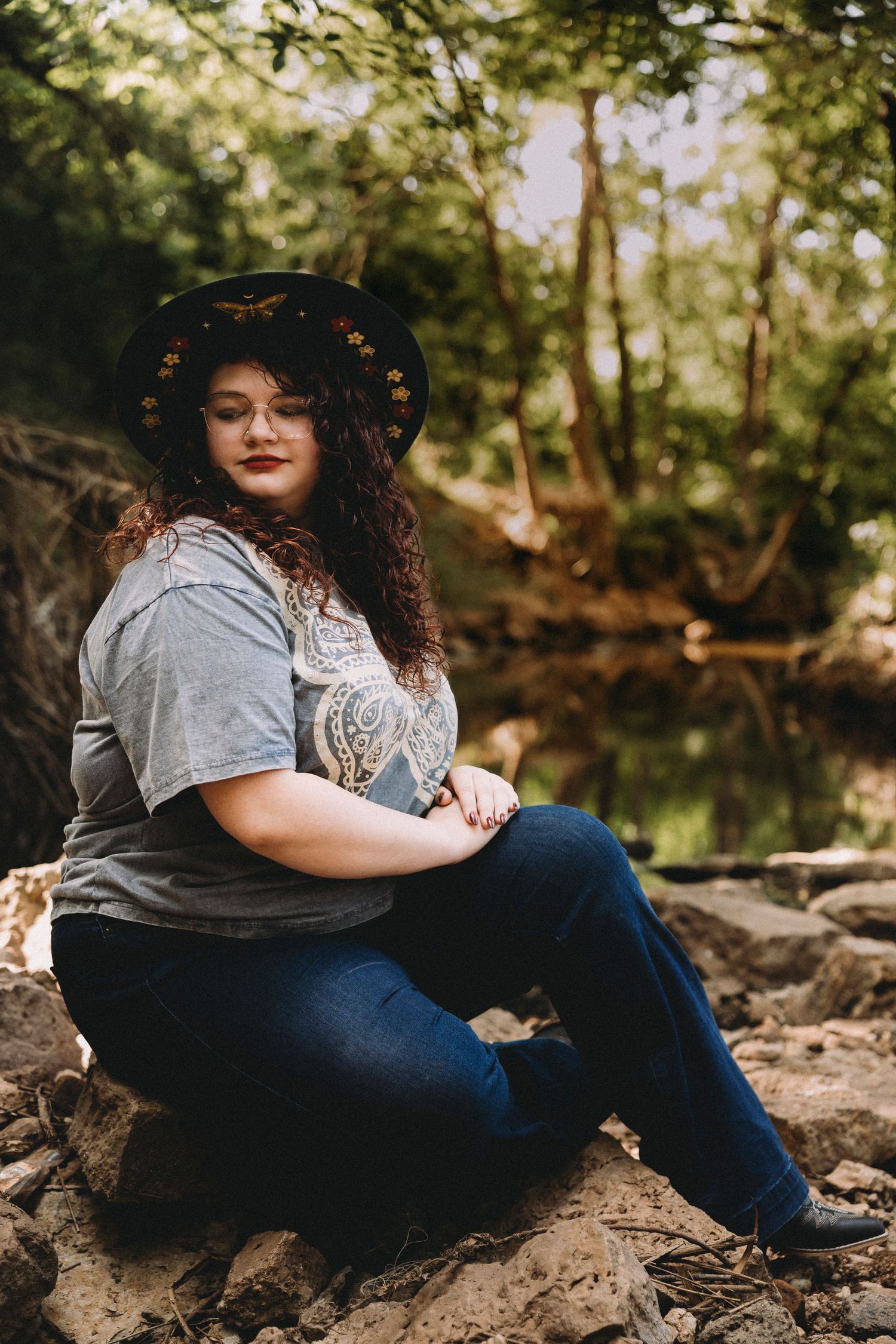 alternative High school senior wearing a black hat while sitting on creek rocks during an outdoor senior portrait session in Abilene, Texas.
