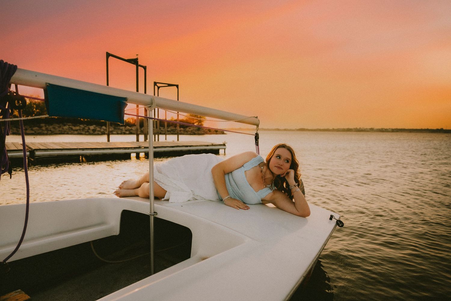 Senior girl posing on a sailboat at sunset during a creative senior portrait session near Abilene, TX.