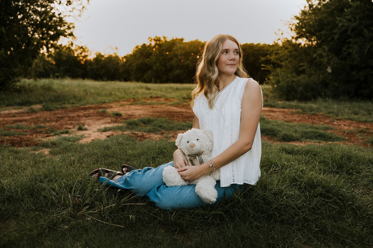 High school senior sitting in a grassy field with her childhood stuffed animal during an outdoor senior photography session in Abilene, Texa