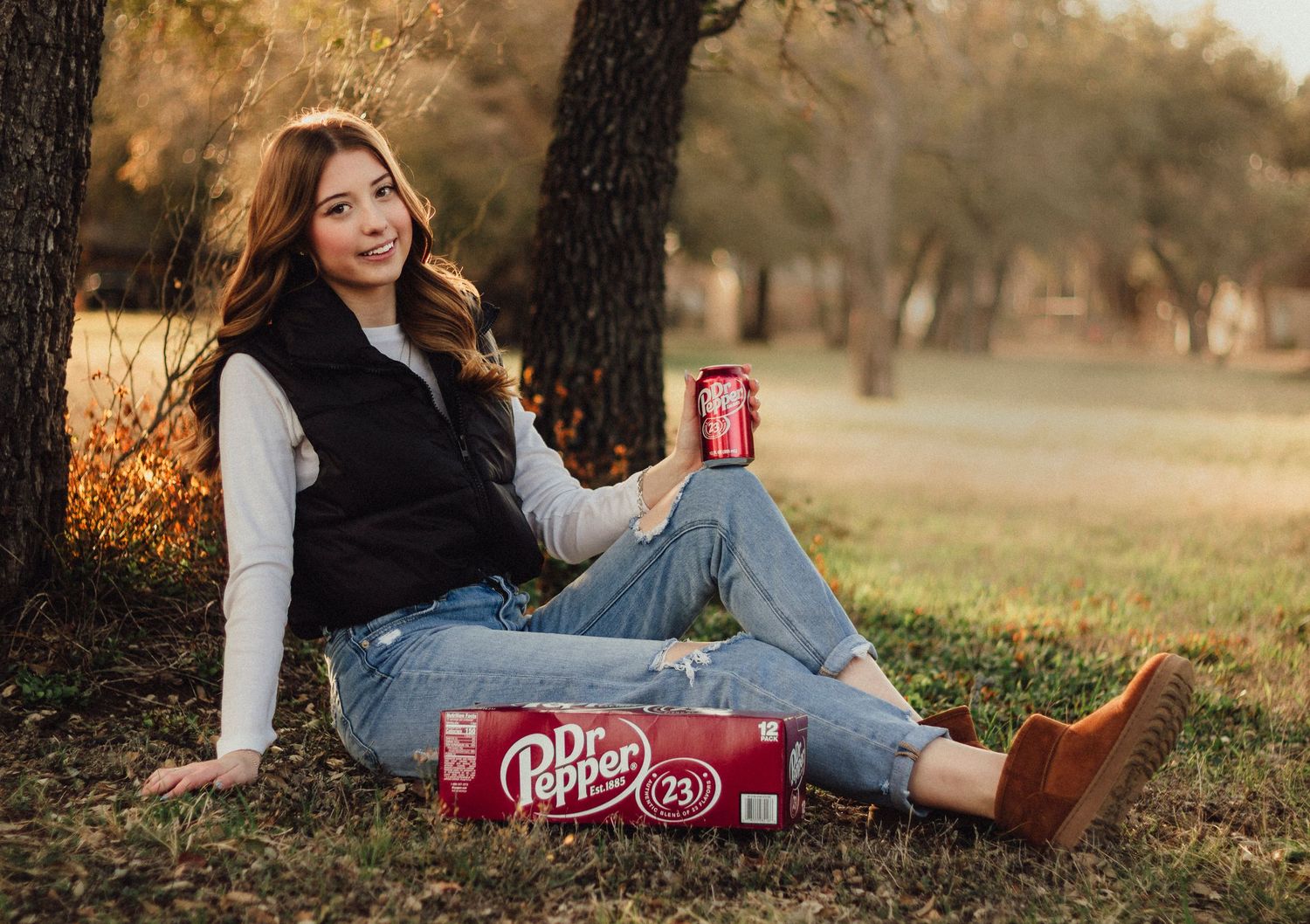 Abilene TX senior photographer capturing a high school senior sitting outdoors at golden hour holding a Dr Pepper, styled in casual denim