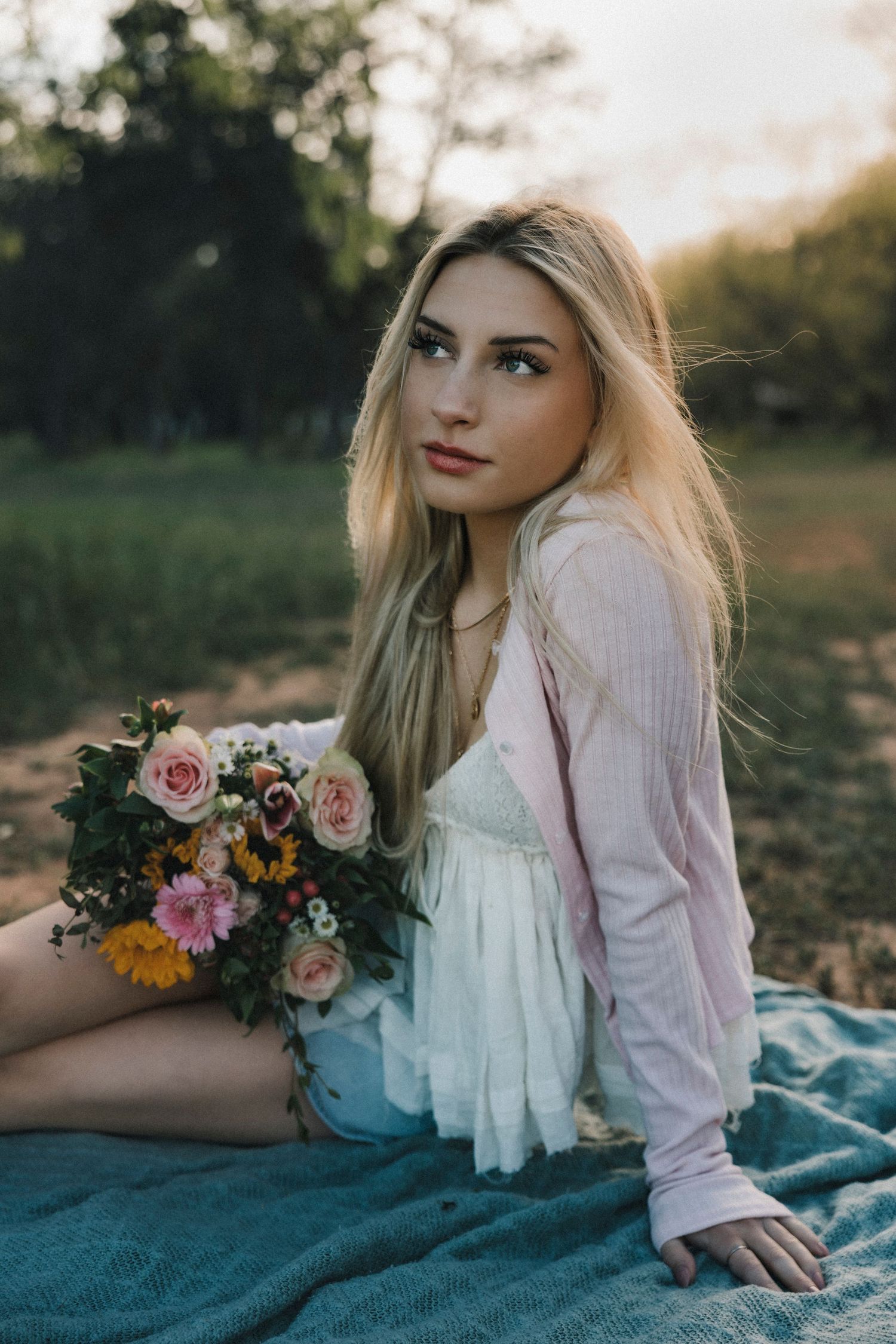 High school senior sitting on a dirt path with sunflowers during a personalized senior photo session in Abilene, Texas